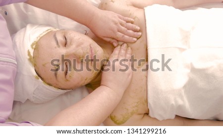 Beautician massages a woman's face with a mask of kiwi or green algae. Asian woman taking spa treatments at the beauty salon. The concept of beauty, body care and health. Day of a cosmetologist.