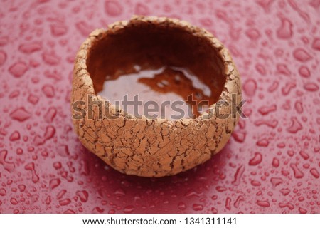 Close-up handmade ceramic cup with cracks
on burgundy with water drops background. Drops of water on a brown surface after a rain.  