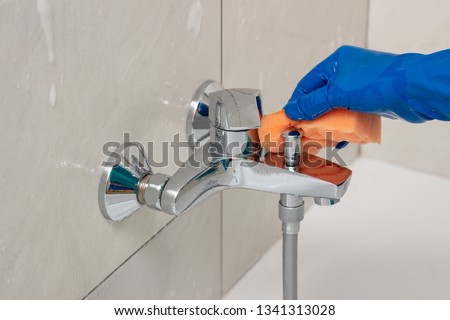 Close-up of the shower faucet and shower head cleaning process from lime scale, white chalk sediment and stains using a commercial soap scum remover. Bathroom cleaning and disinfection, cleanup Royalty-Free Stock Photo #1341313028
