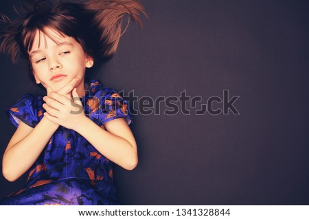 Charismatic girl in a blue dress with abstract orange flowers on a dark background. Place for inscription. child