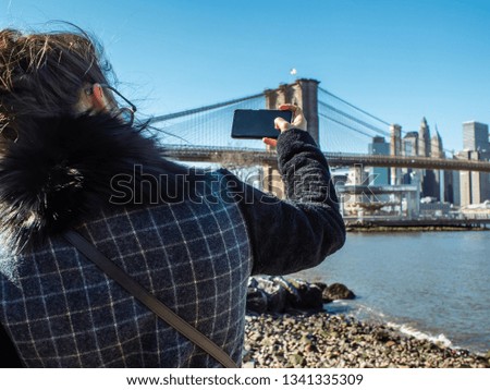 Young Woman tourist by the river in Dumbo taking pictures of Brooklyn Bridge and Cityscape of New York skyline. NY_30_413