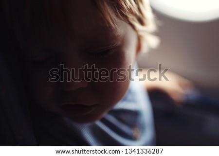 Relaxed little blonde hair toddler boy sleeping in jet airplane sitting next to the window