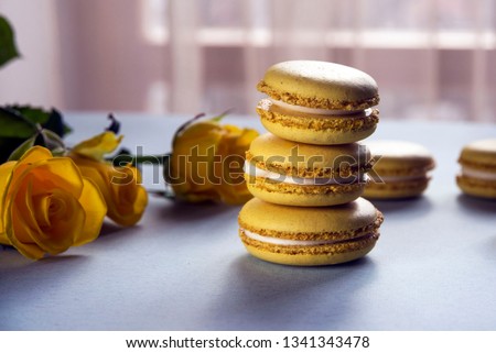 Lemon yellow macaroons on a background of yellow roses. Delicious French dessert. Close-up.