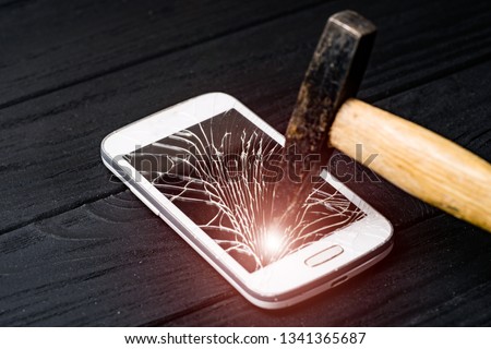 Hammer crashes smartphone and the screen becomes broken on the dark background with light leaks. Damaged mobile phone by a hummer. Close-up