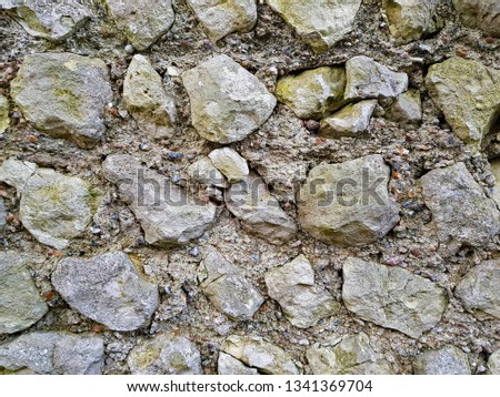 Large and small ,rough, irregularly shaped rocks embedded into a relatively modern cement wall. 