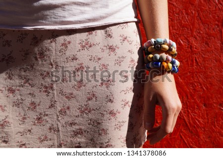 A girl in in the pastel pink floral print skirt, with the handmade ceramic bracelets on her arm. Model with bracelets, on grunge red background. Casual style of woman accessories. 