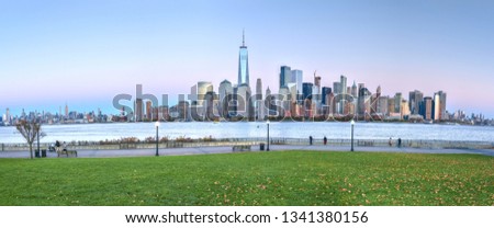 Late afternoon panorama of New York City on the shores of the Hudson River. The foreground includes the green grass of Liberty State Park, across the river in New Jersey.