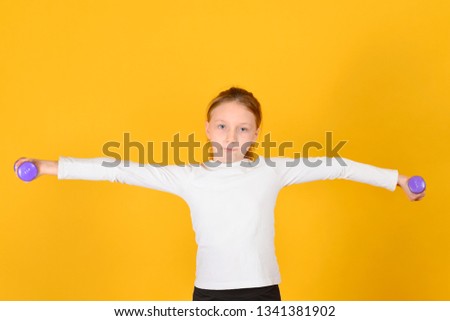 The girl is engaged in fitness with dumbbells, on a yellow background.
