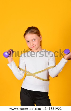 Young and athletic girl with dumbbells and a centimeter at the waist, on a yellow background.