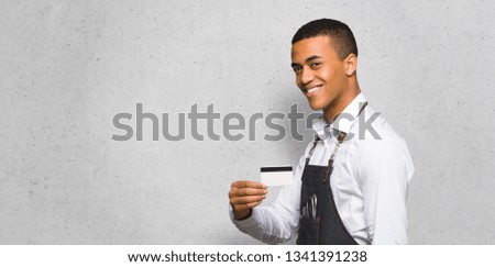 Young afro american barber man holding a credit card on textured wall