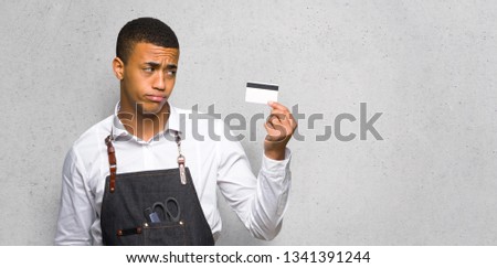 Young afro american barber man taking a credit card without money on textured wall