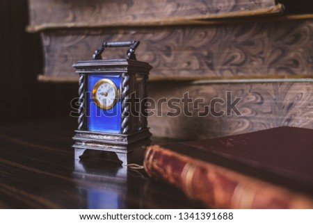 Vintage clock on the table on the background of old books.