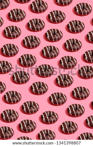 Food design with tasty chocolate glazed donut with white strips on coral pink pastel background top view pattern