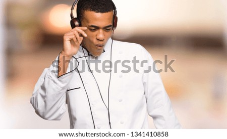 Young afro american chef man listening to music with headphones and dancing on unfocused background