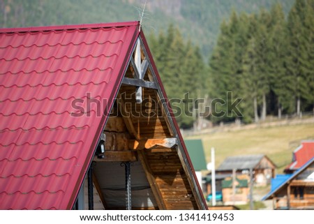 Close-up detail of new modern house top with shingled red roof and wooden sidings on foggy spruce mountains background. Professionally done building and construction work, real estate property.