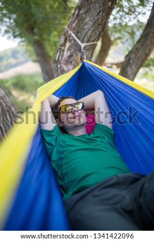 Photo of man in sunglasses lying in hammock in forest