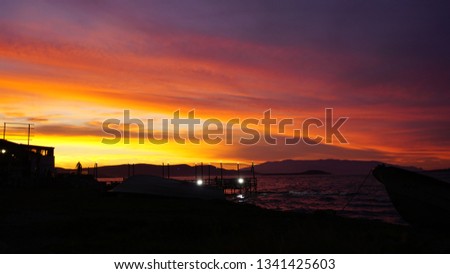 Dramatic sunset landscape at Urla, Izmir, Turkey. Beautiful blazing sunset landscape over bright blue sea and orange cloudy sky above it with awesome golden rays of sun light reflection on calm waves.