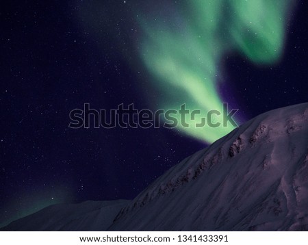 Magical green aurora shining above the snowcapped mountains on Svalbard. 