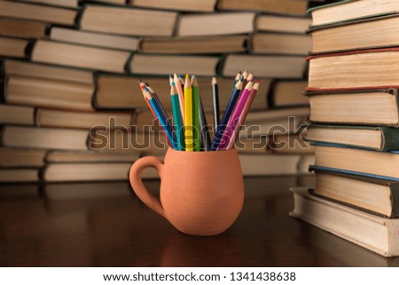 colored pencils in a mug on the background of books