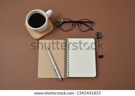 Mockup workspace with office supplies, pen, coffee cup, notepad and glasses on brown background. Flat lay, top view, copy space
