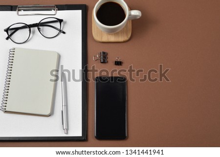 Mockup workspace with blank clip board, office supplies, pen, smartphone, notepad , coffee cup and spectacles on brown background. Flat lay, top view, stylish concept