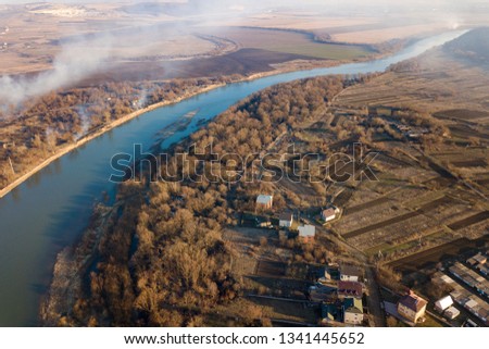 Aerial top view of river flowing through town. Rural landscape of residential house roofs, roads and tree tops on spring or autumn day. Drone photography.