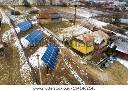 Aerial top view of stand-alone blue shiny solar photo voltaic panel systems producing renewable clean energy in rural residential area on sunny winter day.