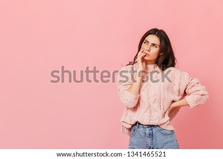 Attractive lady in bright outfit is thinking about new idea. Woman in sweater posing thoughtfully on pink background