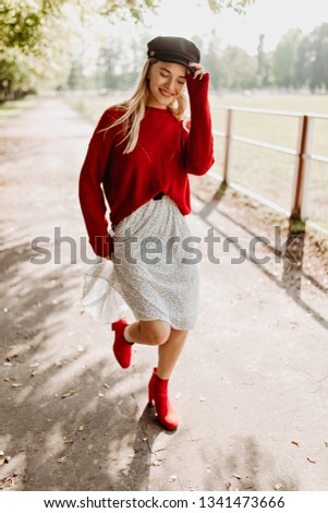 Beautiful girl wearing trendy red shoes and white dress in the forest. Charming blonde feeling happy under the sun on the street.