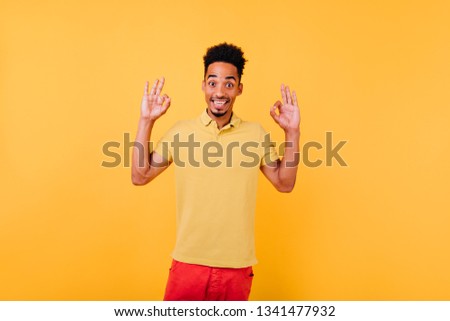 Amazed cute man in summer t-shirt posing on yellow background. Studio portrait of excited guy with black hair.