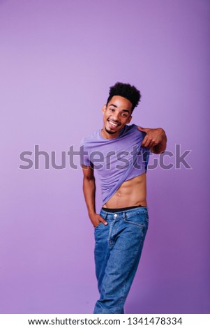 Romantic african model taking off his t-shirt. Indoor photo of laughing cute black man.