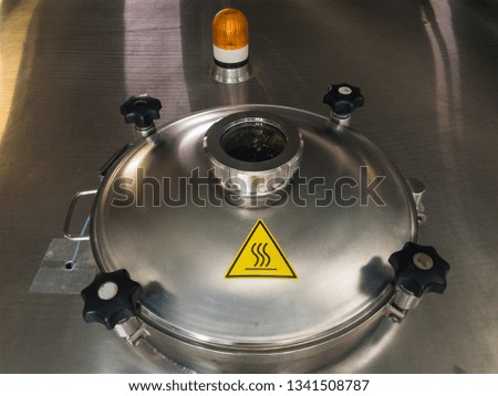 Metal door of stainless steel beer brew tank with viewing glass  with  yellow warning light and sign about overheating