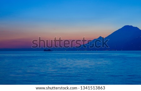 Sunset on sea, blue waters with strip of red Golden sky, huge mountain in shade