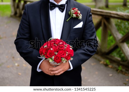 Groom standing in park and holding wedding bouquet of roses. Celebration, holidays and gifts concepts. Wedding day