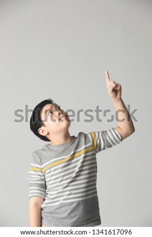 Asian cute teenager boy in gray sweater Teenage boy points up over gray background, half body with copy space .