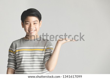 Asian cute teenager boy in gray sweater presenting something on hand over gray background, half body with copy space .