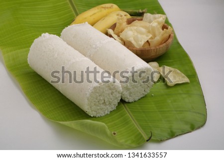 puttu south indian breakfast-front view of two slices of puttu with banana and pieces of pappadam on tender banana leaf with white background

