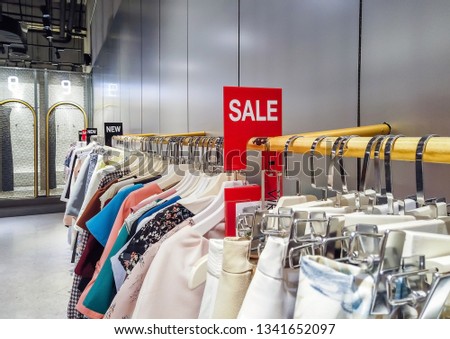 Red sale sign on clothing rack in modern shopping mall or department store. Retail shop promotional event, business marketing advertising concept 