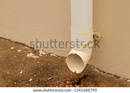 An old plastic gutter drainage pipe mounted to the wall of a house. 