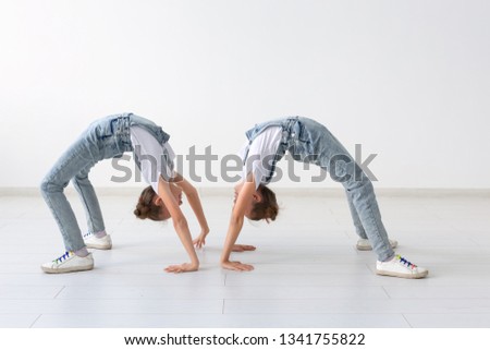 people, children and acrobatic concept - little twin sisters doing exercises on white background
