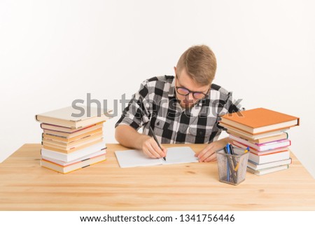 People, knowledge and education concept - Happy student sits at the table and makes notes in a notebook
