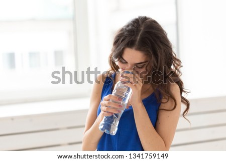Sport, healthy lifestyle, people concept - young woman drinking water after sport