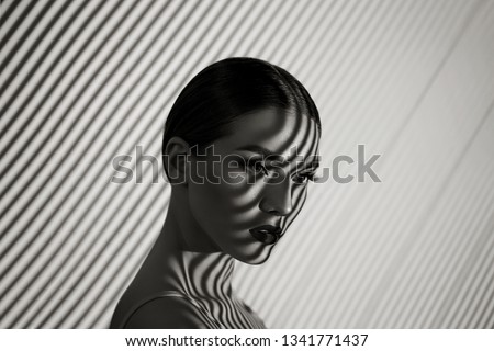 Black and white portrait of a beautiful young girl with a shadow pattern on the face and body in the form of stripes.fashion, beauty, makeup, cosmetics, beauty salon, style, personal care, posture. Royalty-Free Stock Photo #1341771437