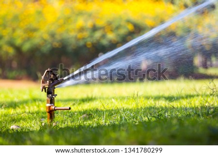 Water sprinkler irrigation. / Irrigation System Watering the green grass with  blurred background. / Sprinkler head watering the bush and grass in the garden. Royalty-Free Stock Photo #1341780299