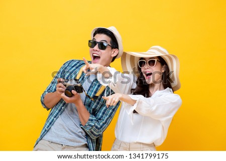 Happy excited young Asian couple tourists in colorful yellow background
