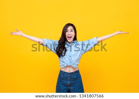 Cheerful pretty Asian woman with open hands studio shot isolated on yellow background