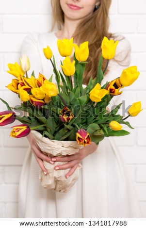 Beautiful young woman with tulips on white wall background