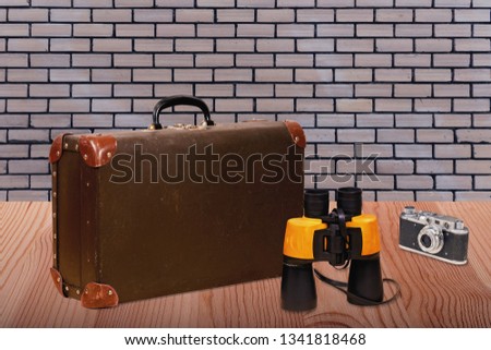 Accessories for the rest. Binoculars, a suitcase and a camera on a wooden table against a brick wall