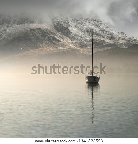 Beautiful landscape image of sailing yacht sitting still in calm lake water with mountain looming in background during Autumn Fall sunrise