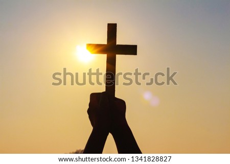 silhouette human hands praying to the GOD while holding a crucifix symbol with bright sunbeam on the sky